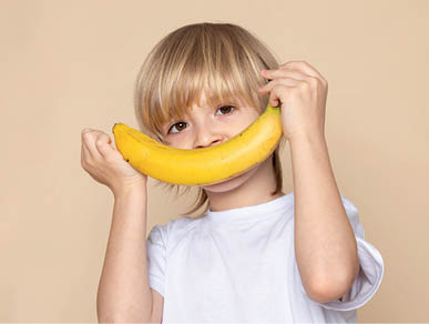 a front close up portrait view blonde boy smiling cute sweet with banana in white t-shirt on the pink desk
